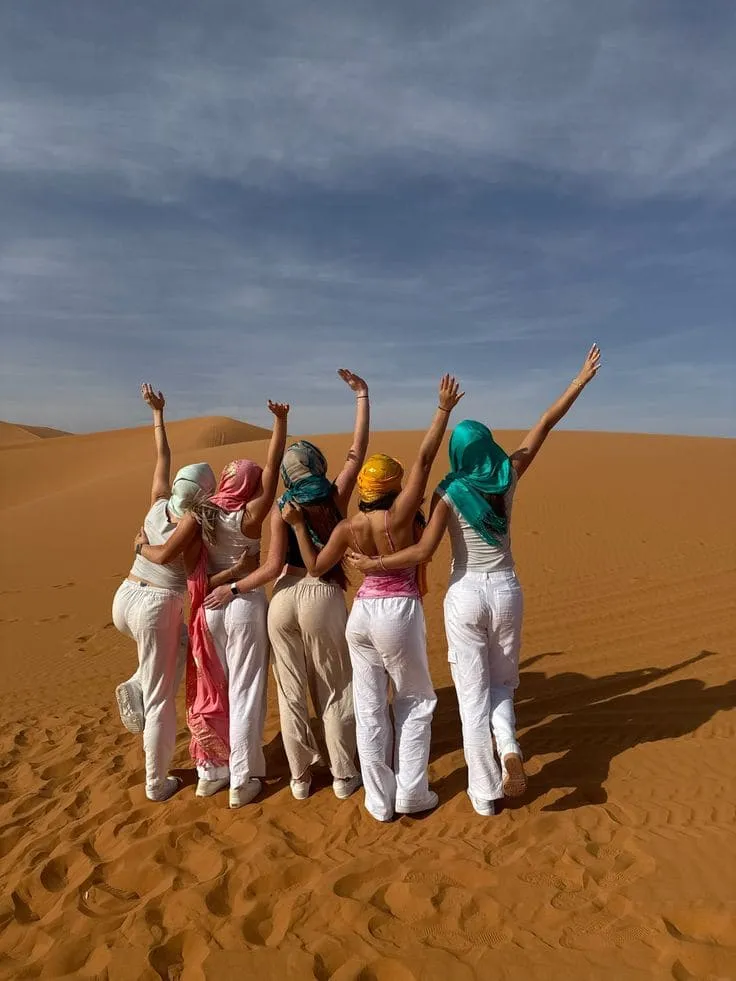 Friends Celebrating in the Sahara Dunes – Merzouga Desert Group of happy women raising their arms on the golden sand dunes of Merzouga, Morocco