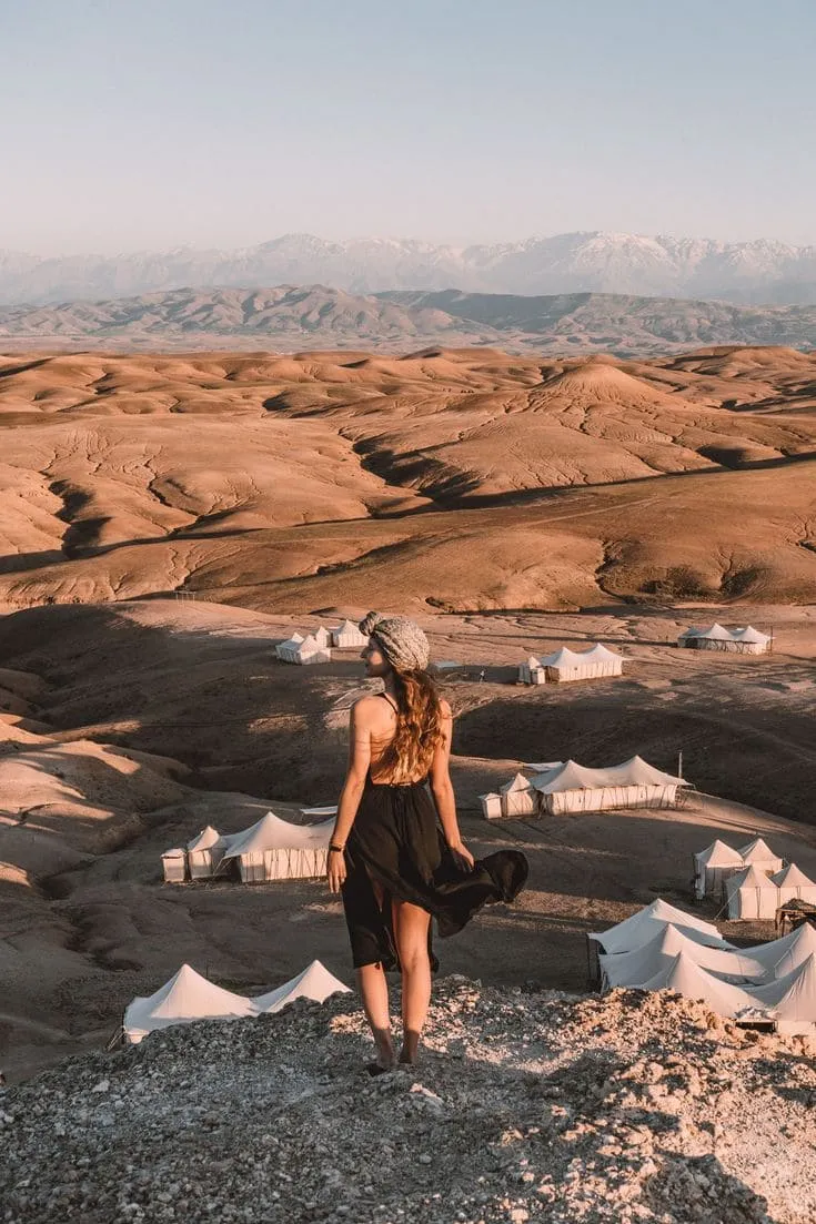 Panoramic View of Agafay Luxury Desert Camp, Morocco Woman overlooking white luxury tents and desert landscape in Agafay near Marrakech