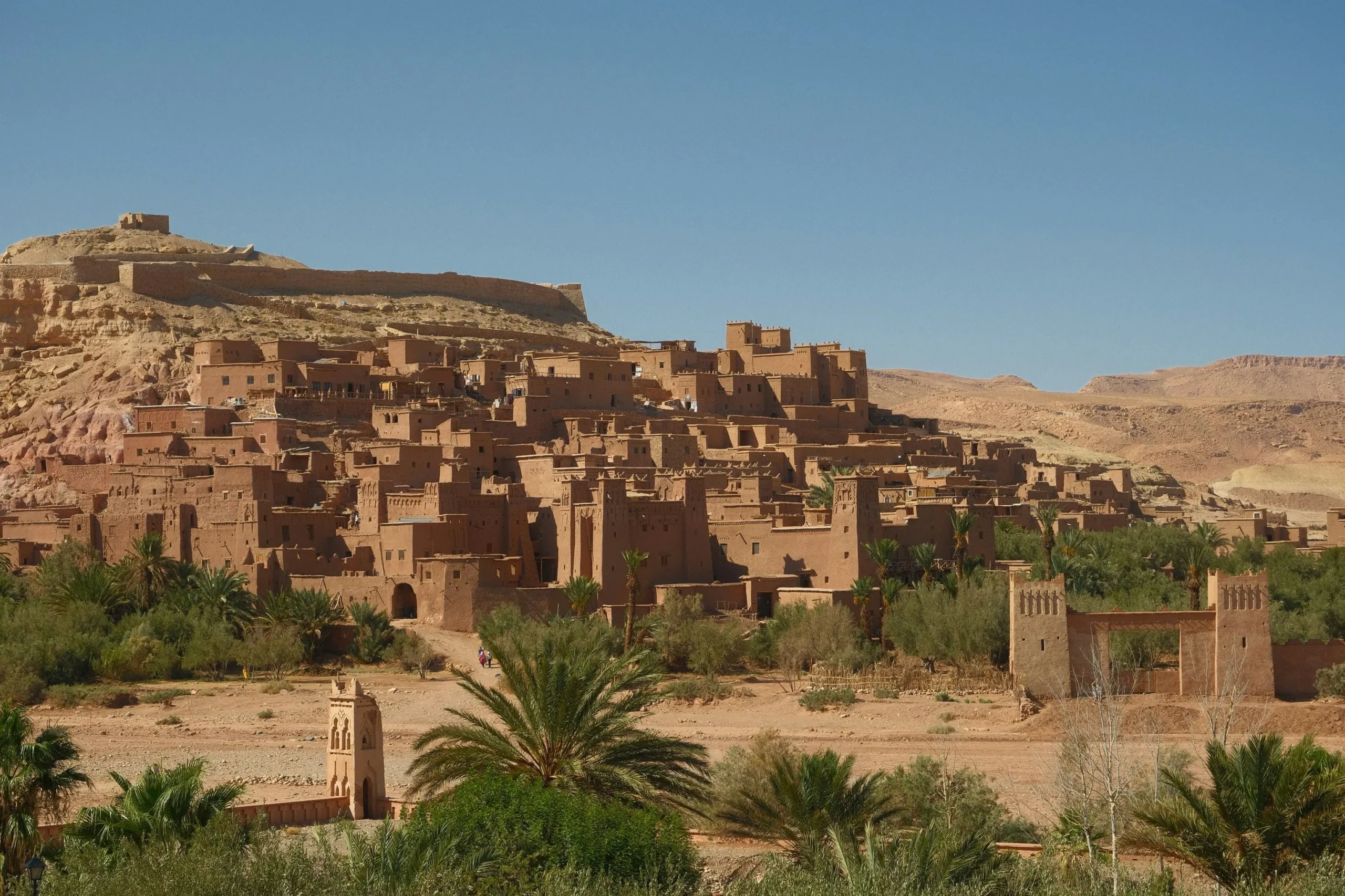 Wide view of Aït Benhaddou fortress and kasbah rising from the desert with palm groves below